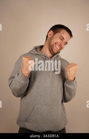 The man, with a wide grin, lifts his fists in celebration, expressing immense joy. This victorious gesture reflects a moment of success and personal Stock Photo