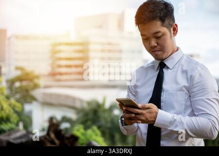 Successful Asian man, software developer, smiles testing app. Director outside office, serious about Stock Photo