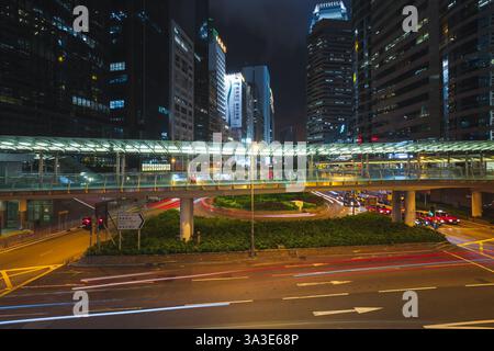 Hong Kong - July 19, 2017: A vibrant night scene showcasing urban architecture, light trails, and a modern elevated pedestrian bridge in the bustling Stock Photo