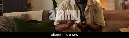 Elderly man using smartphone while sitting on comfortable couch in cozy setting with home decor around. Focused on screen, suggesting involvement in digital communication Stock Photo