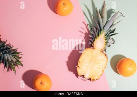 Fresh fruits, half a pineapple and oranges, on a colorful background with strong shadows. Top view, flat lay, copy space. Stock Photo