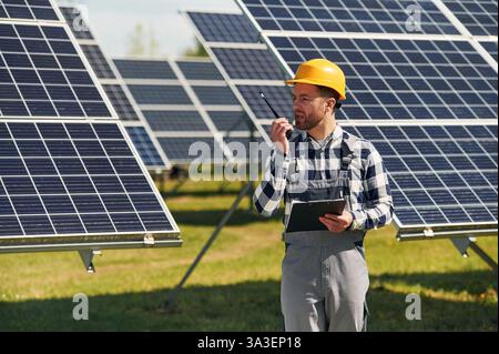 Communication by using walkie talkie. Engineer with photovoltaic solar panels outdoors at daytime. Stock Photo