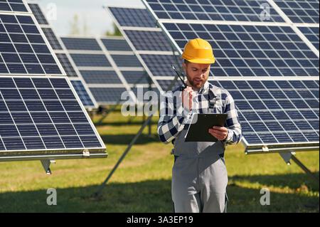 Communication by using walkie talkie. Engineer with photovoltaic solar panels outdoors at daytime. Stock Photo