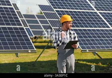 Communication by using walkie talkie. Engineer with photovoltaic solar panels outdoors at daytime. Stock Photo