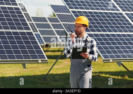 Communication by using walkie talkie. Engineer with photovoltaic solar panels outdoors at daytime. Stock Photo