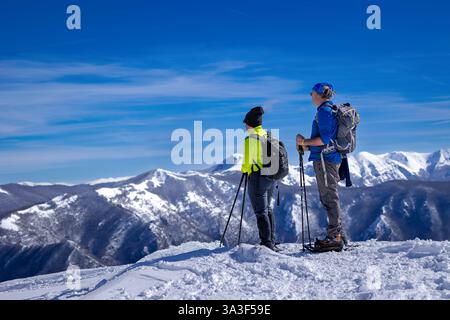 Two sporty men snowshoe on the snow with snowshoes and poles, in the background, the snowy mountains. Stock Photo