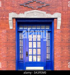 Cobalt blue door with glass panes highlighted by a diamond-shaped brick pattern and geometric stone framing. Stock Photo