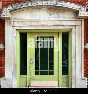 Vintage lime green glass-paneled door set within an ornate stone and red brick facade, featuring decorative architectural details. Stock Photo