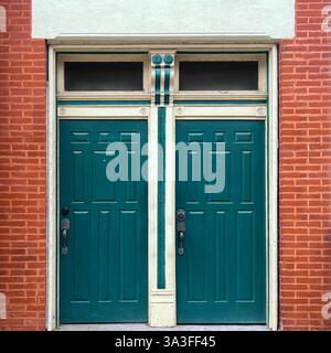 Vintage double green doors with decorative trim and transom windows set in a red brick facade. Stock Photo