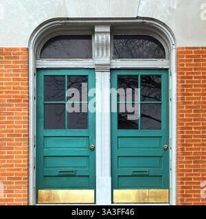 Elegant teal double doors with glass panes, framed by an arched stone facade and orange brick walls. Stock Photo
