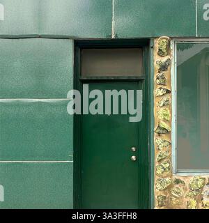 A deep green door set in a textured stone and metal-paneled facade, blending mid-century urban design with natural elements in Chicago Stock Photo
