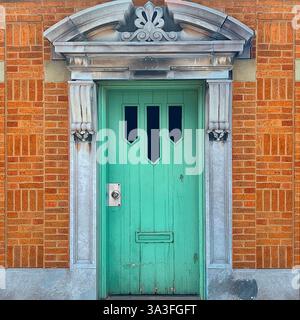 Mint-green door with three elongated cutout windows, framed by an ornate stone pediment and decorative columns, set in orange brick facade. Stock Photo