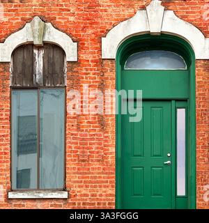 A bright green door with a modern vertical window stands out against the aged orange brick facade in Chicago Stock Photo