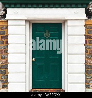 Green wooden door set within a white classical-style entrance, framed by a rustic stone wall, featuring an ornate door knocker in Chicago Stock Photo