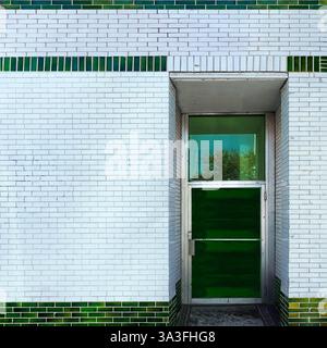 Green glass door set within a striking white and green-glazed brick facade, reflecting the surrounding in Chicago Stock Photo