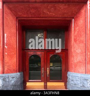 Red double door with ornate woodwork set within a polished red marble facade, reflecting the elegance of historic architecture in Chicago Stock Photo
