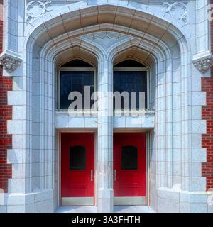 A pair of red doors set within a grand Gothic-style stone archway, framed by intricate architectural details on a historic brick building. Stock Photo