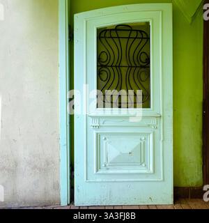 An elegant pale green vintage door with intricate ironwork and classic panel details stands slightly open in a historic building in Łódź, Poland Stock Photo