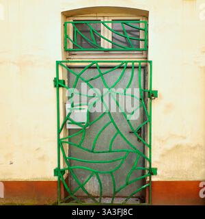 A creatively designed green metal security gate with an abstract, wavy pattern guards an old industrial entrance in Łódź, Poland Stock Photo