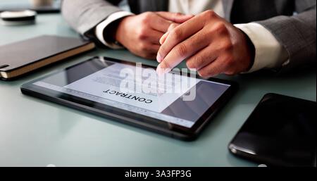 Focused young man reviewing contract paperwork on computer in office. Stock Photo