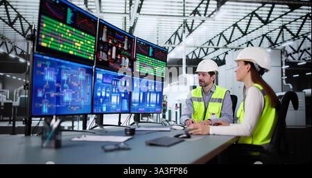 Operators and engineers monitor SCADA system using control in factory. Woman and man monitor process technology on screen. Stock Photo