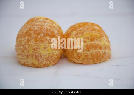 Two mandarins, whole and without skin, with orange rind, lying on a white surface, front view. Stock Photo