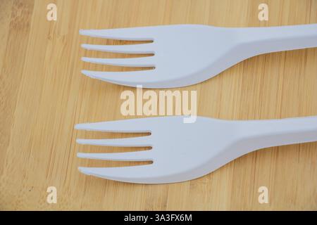 Two white plastic forks, laying flat side by side on the table. The forks are the same size as your own hand and have three prongs at one end with no Stock Photo