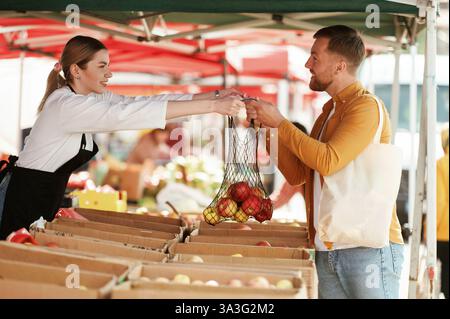 Taking apples. Man is buying products on the street market or bazaar from woman. Stock Photo