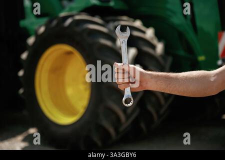 Close-up of hand holding wrench in front of tractor. Stock Photo