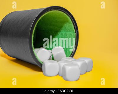black leather cup with blank white dice isolated on a yellow background for board games and casino Stock Photo