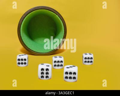 close up showing five dice all showing number six against an empty dice cup isolated on a yellow background Stock Photo