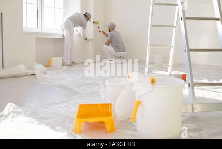 Team of two men construction workers painting walls with paint rollers, doing house repair  Stock Photo