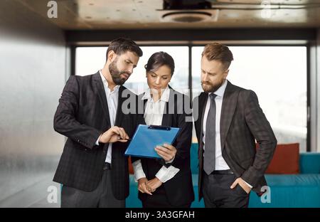 Busy business group, three colleagues meeting talk in modern office hall near big window, working  Stock Photo