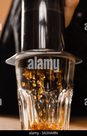 Falling coffee drops in cup close-up. Aeropress coffee. Process of pouring coffee in cup. Barista is pushing aeropress for pouring coffee drops Stock Photo