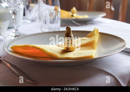 Elegant Easter table setting with a gold foil-wrapped chocolate bunny on a yellow napkin, placed on fine dinnerware. A festive and refined ambiance. Stock Photo