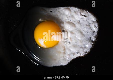 An egg in a cast iron pan, raw on the left side and cooked on the right side Stock Photo