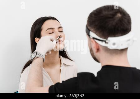Rhinoscopy of woman nose. Consultation with ENT doctor. Otolaryngologist examines girl nose before procedure of endoscopy of nose Stock Photo