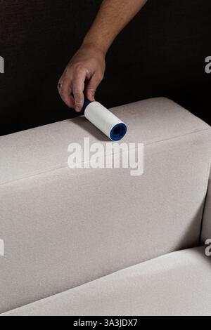 Cleaning couch using lint roller from cat and dog hair. Cleaner is removing lint from sofa using cleaning roller close-up Stock Photo