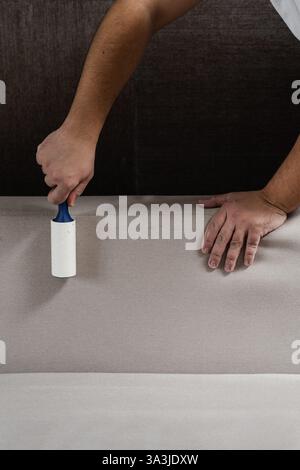 Cleaning couch using lint roller from cat and dog hair. Cleaner is removing lint from sofa using cleaning roller close-up Stock Photo