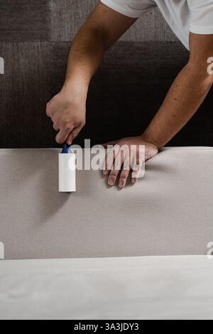 Cleaning couch using lint roller from cat and dog hair. Cleaner is removing lint from sofa using cleaning roller close-up Stock Photo