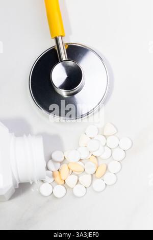 Close-up image of various white and beige medical pills scattered on a reflective surface, accompanied by a stethoscope. The image conveys themes of h Stock Photo