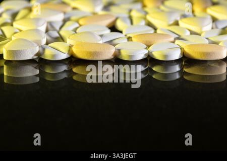 Macro photograph of round tablets in white and yellow, beautifully reflected on a black glossy surface, illustrating pharmaceutical or health-related Stock Photo
