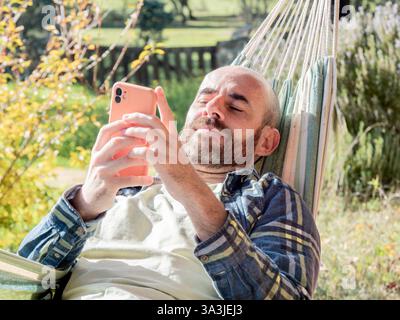 Man relaxing in hammock using smartphone outdoors Stock Photo