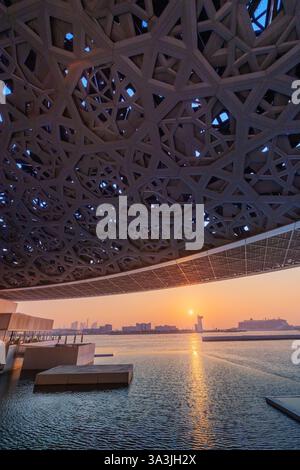17 January 2025, Louvre museum Abu Dhabi, UAE: Museum dome reflecting sunset light in the water at dusk Stock Photo
