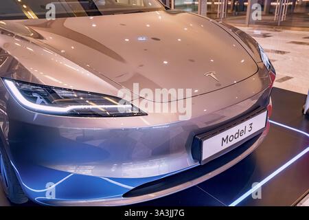 17 January 2025, Abu Dhabi, UAE: Modern gray Tesla Model 3 electric car parked on display with headlights illuminating showroom floor Stock Photo