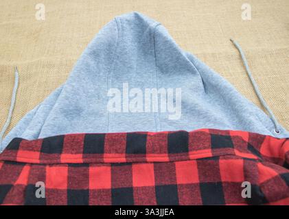Hood of an oversized hoodie with flannel material, on top of a grey sweatshirt and red plaid fabric. Stock Photo