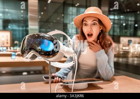 Surprised woman looking at virtual reality headset in modern electronics store Stock Photo