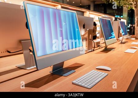 17 January 2025, Abu Dhabi, UAE: Row of desktop iMac computers showing colorful abstract images on screen in modern Apple electronics store Stock Photo