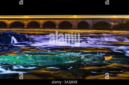 Flowing river under illuminated bridge at night with vibrant reflections and smooth water textures Stock Photo