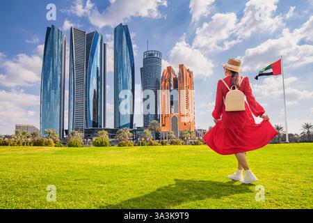 Happy woman tourist wearing a red dress, hat and sunglasses, with United Arab Emirates flag in background Stock Photo